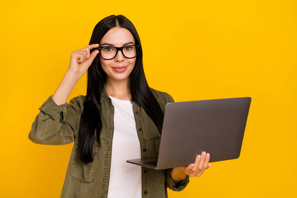 Photo of nice millennial lady hold laptop wear eyewear khaki shirt isolated on yellow background. - Foto, imagen