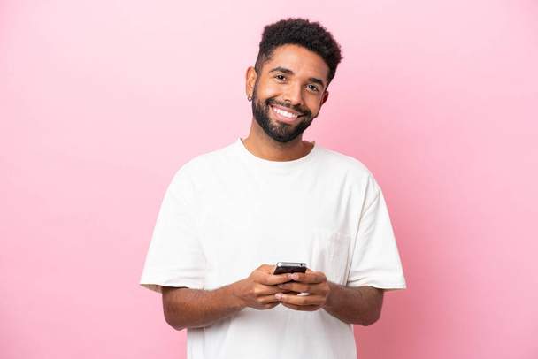 Joven brasileño aislado sobre fondo rosa enviando un mensaje con el móvil - Foto, Imagen