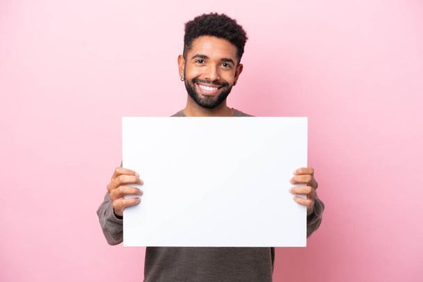 Young Brazilian man isolated on pink background holding an empty placard with happy expression - Foto, immagini