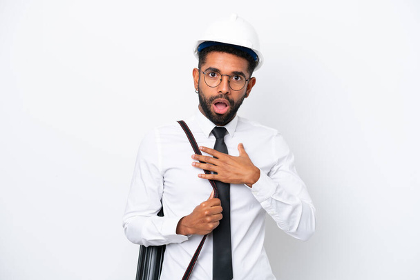 Young architect Brazilian man with helmet and holding blueprints isolated on white background surprised and shocked while looking right - Photo, Image