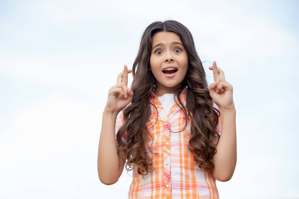 Terrified teen girl keeping fingers crossed sky background, copy space. - 写真・画像