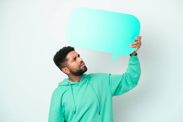 Young Brazilian man isolated on white background holding an empty speech bubble and with sad expression - Photo, image