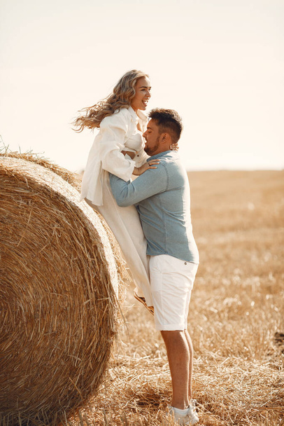 Close up of a young couple sitting at the wheat field. People sits on haystack on meadow and embraces. - Фото, зображення