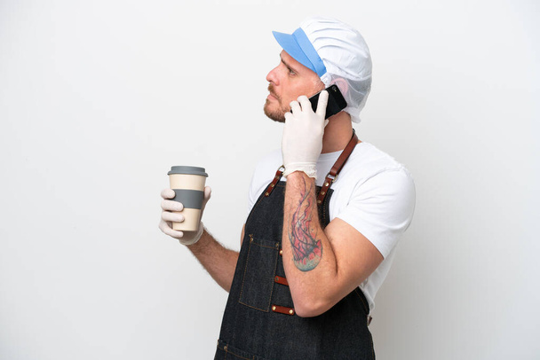 Ένας ψαράς που φοράει ποδιά απομονωμένη σε λευκό φόντο κρατώντας καφέ για να τον πάρει και ένα κινητό - Φωτογραφία, εικόνα