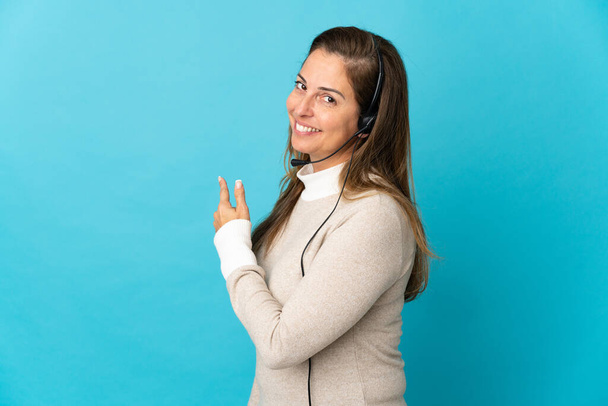 Young telemarketer woman over isolated blue background pointing back - Foto, imagen