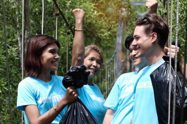 Grupa wolontariuszy w niebieskim t-shircie trzyma worek na śmieci, podnoszą pięści, sprzątają i zbierają śmieci, by wspólnie zmniejszyć zanieczyszczenie środowiska.. - Zdjęcie, obraz