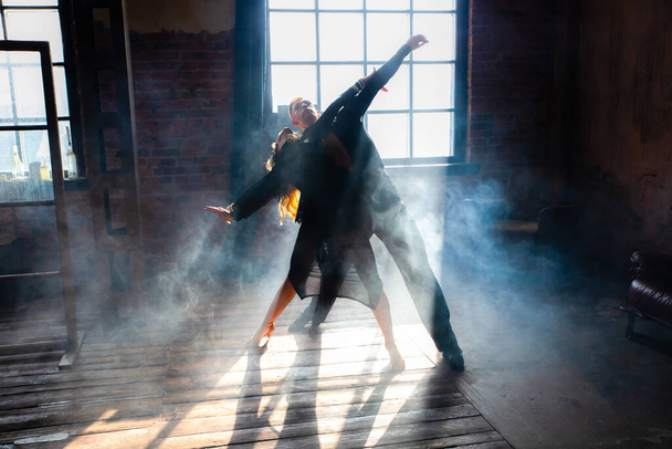 Két profi táncos táncol a tetőtéri stúdióban. Gyönyörű művészeti előadás, erős füsttel. Sport élet koncepció. Szenvedély és érzelmi tánc. - Fotó, kép