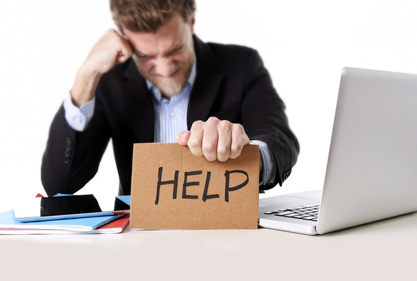 attractive businessman working in stress at computer holding help cardboard sign - Photo, Image