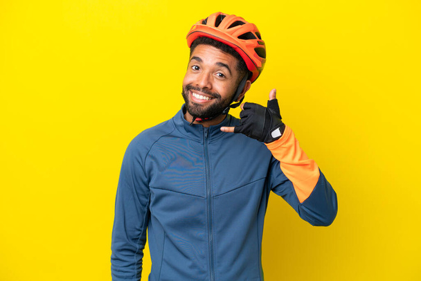 Junger brasilianischer Radfahrer, isoliert auf gelbem Hintergrund, macht Handygesten. Rufen Sie mich zurück - Foto, Bild