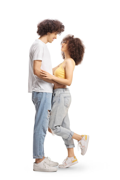 Full length profile shot of casual young couple in love hugging and looking at each other isolated on white background - 写真・画像