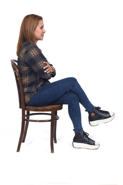 Seitenansicht einer Frau auf Stuhl sitzend, Beine und Arme auf weißem Hintergrund gekreuzt - Foto, Bild