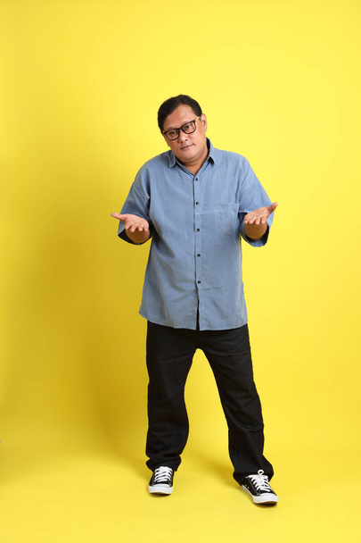 The adult Asian man with blue shirt standing on the yellow background. - Фото, изображение