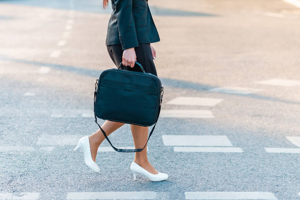 Ноги деталі ділової жінки на шляху до офісу, ходьба на відкритому повітрі, що тримає футляр для ноутбуків, одягнений у діловий костюм та високі підбори.
. - Фото, зображення