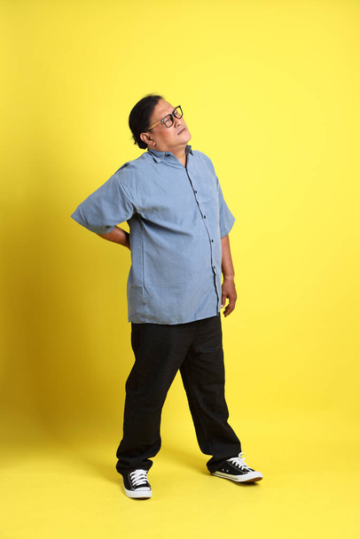 The adult Asian man with blue shirt standing on the yellow background. - Photo, image