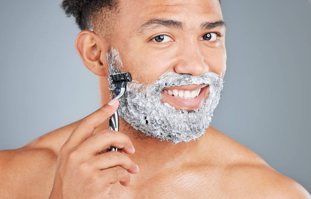 Studio portrait of a handsome young man shaving against a grey background. - Photo, Image