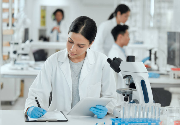 Shot of a young woman making notes in her lab. - Foto, Imagen