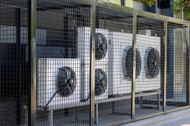 Sistema compresor de aire acondicionado en un edificio moderno protegido por una valla metálica. - Foto, imagen