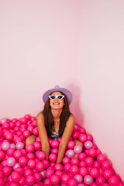 Grappige mooie jonge vrouw die plezier heeft in het zwembad met roze plastic ballonnen. Geïsoleerde roze kleur achtergrond. Monochromatisch concept. - Foto, afbeelding