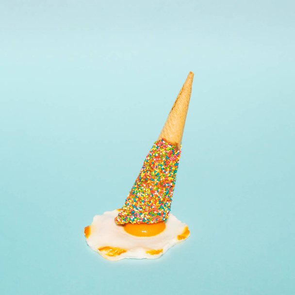 Overhead colorful ice cream cone and poached egg on pastel blue background. Minimalistic summer food concept. - Fotoğraf, Görsel