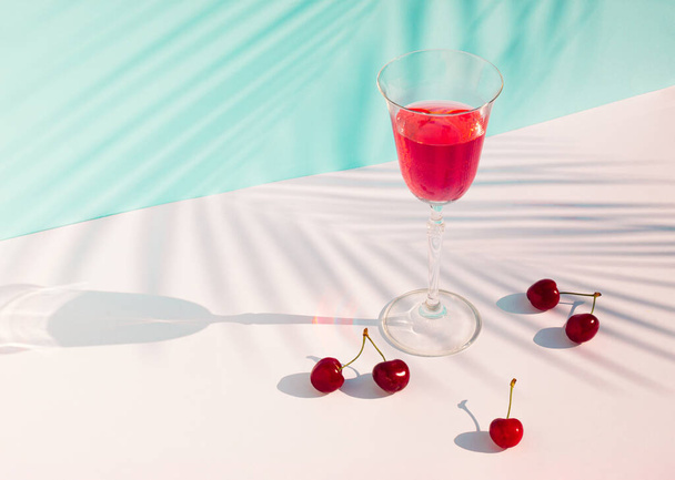Creative summer composition with cherries, glass of juice and palm leaf shadow. Minimal summer drink concept. - Фото, зображення