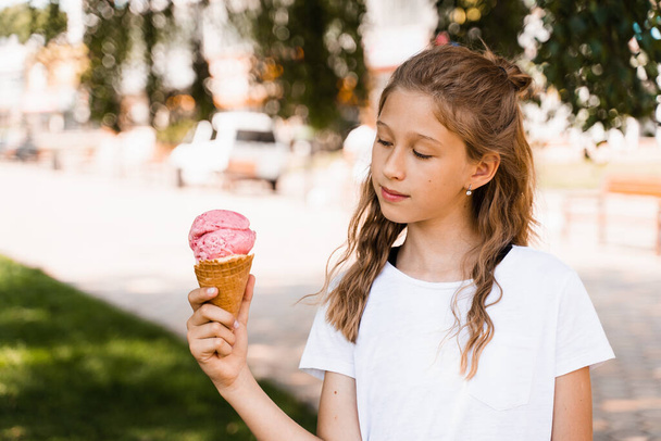 Happy child girl with ice cream cone in summer park. Attractive girl holding sweets ice cream cone and smiling - Foto, Imagem