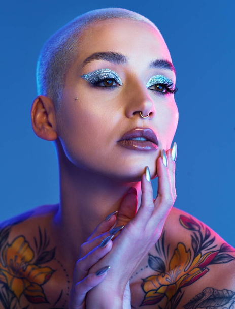 Studio shot of an attractive young woman wearing edgy makeup against a blue background. - Foto, Imagem