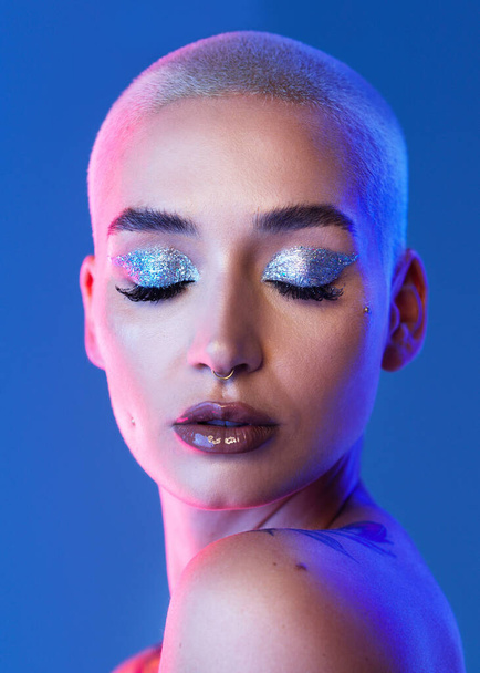 Studio shot of an attractive young woman wearing edgy makeup against a blue background. - Photo, image