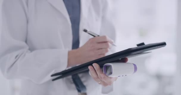 Closeup of a doctor writing covid patients chart during a checkup holding a thermometer. Taking temperature reading measurements and adhering to corona virus pandemic protocol. - Video