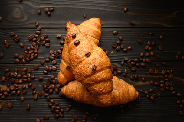 Croissants with coffee beans on a wooden background. - Photo, Image