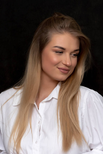 Молода красива блондинка 20-25 років у білій довгій сорочці на чорному текстурованому фоні
. - Фото, зображення