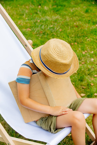 Engraçado menino com um livro senta-se na cadeira ao ar livre - Foto, Imagem