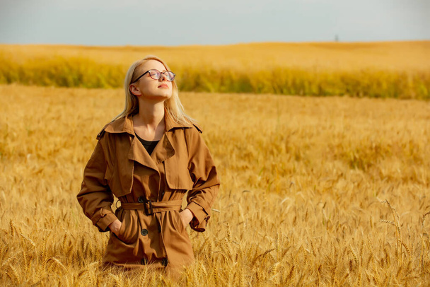 Stylish girl in eyeglasses and cloak in wheat field - 写真・画像