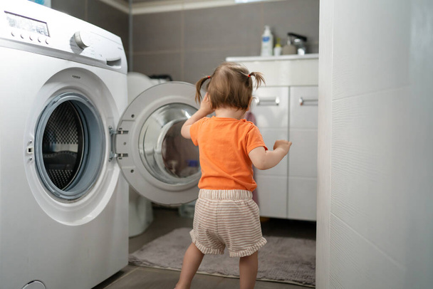 Ένα κορίτσι μικρό καυκάσιο μικρό παιδί κόρη στέκεται στο πλυντήριο στην τουαλέτα ανοίγοντας ή κλείνοντας την πόρτα εξετάσει και να μάθουν την πρώιμη ανάπτυξη και μεγαλώνοντας σκανταλιάρικο έννοια αντίγραφο χώρο - Φωτογραφία, εικόνα
