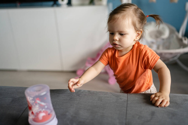 une fille petit bébé caucasien tout-petit jouant au canapé-lit à la maison debout près de la bouteille d'eau seule personne réelle copier l'espace grandir l'enfance et le développement concept copier l'espace - Photo, image