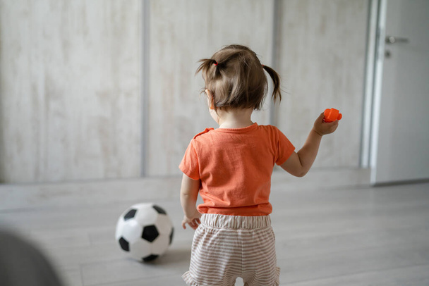 Bir kızın, turuncu tişört giyen küçük beyaz bir kızın futbol topunun yanında dikilirken ya da yürürken gelişim sporu konsepti fotokopi alanı - Fotoğraf, Görsel