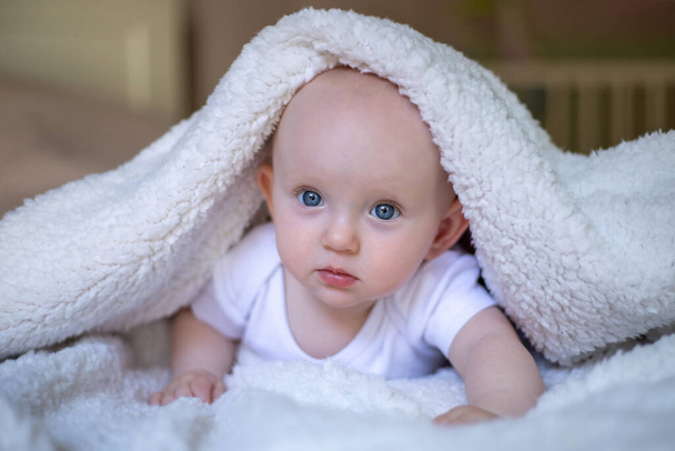 smiling baby looking at camera under a white blanket, towel. selective focus - Photo, image