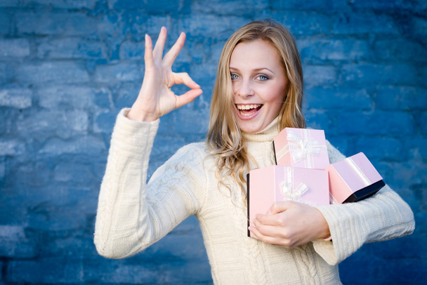 attractive blond young woman in woolen sweater receiving presents having fun happy smiling on blue brick wall background - Photo, Image