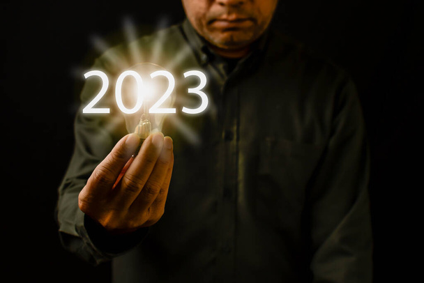 Bright lights give hope to small businesses. 2023 New Year concept, Copy space, Close-up, A man holding a light bulb is the concept of the startup that drives global business. Black Blurred background - Fotoğraf, Görsel