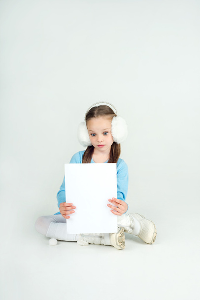 Cute girl in winter clothes with a white blank paper sheet. - 写真・画像