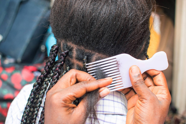  Жіноча рука перукаря виготовляє плетіння на плечах на голові молодої дівчини, створюючи творчу органічну зачіску з гребінцем. - Фото, зображення