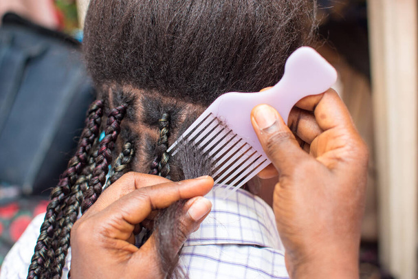  Жіноча рука перукаря виготовляє плетіння на плечах на голові молодої дівчини, створюючи творчу органічну зачіску з гребінцем. - Фото, зображення
