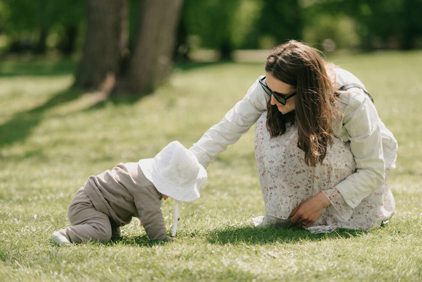 Mladá matka si hraje se svou sedmiměsíční dcerou na louce. Malá holčička se plazí po trávě. - Fotografie, Obrázek