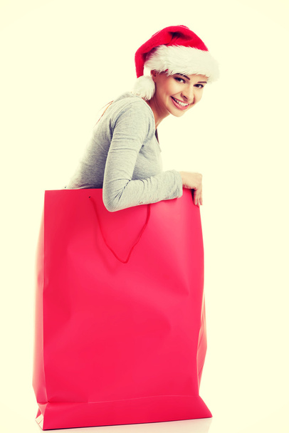Beautiful girl wearing santa hat in red shopping bag. - Фото, изображение