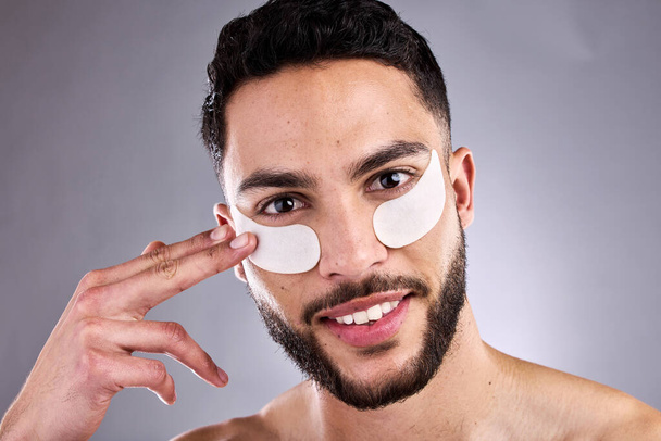 a handsome young man wearing under-eye patches against a grey background. - 写真・画像