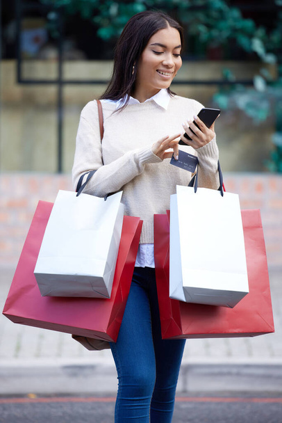 a woman using her cellphone while walking outside with shopping bags. - Foto, imagen