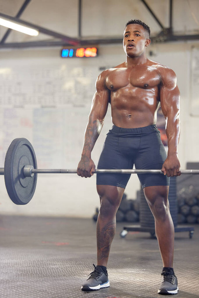a muscular young man exercising with a barbell in a gym. - 写真・画像