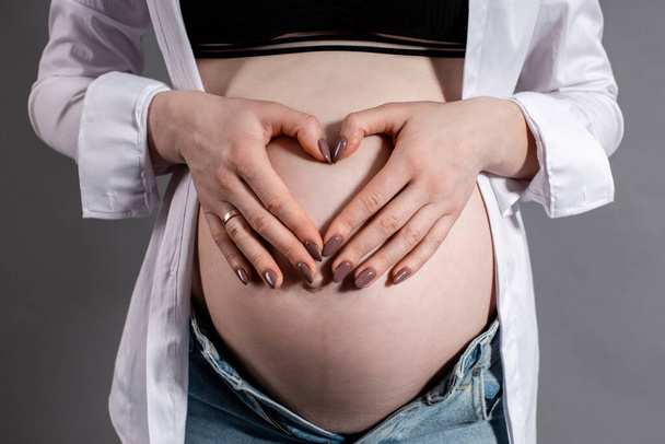 raskaana oleva nainen seitsemännen raskauskuukauden aikana pitää käsiään vatsallaan ja taittaa ne sydämen muotoon. lähikuva kuva - Valokuva, kuva