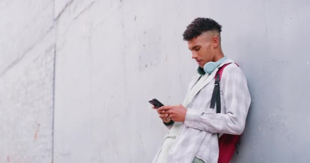 Trendy guy with headphones using his phone outside. Young male student in the millennial age happy to be connected while on the go, listening to music playing online games and texting on social media. - Materiał filmowy, wideo
