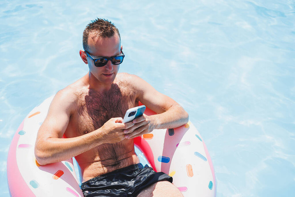 Atraktivní muž odpočívá na nafukovacím prstenu v bazénu. Muž v bazénu mluví po telefonu. dovolená a volný čas koncept - Fotografie, Obrázek