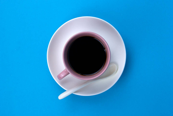 An isolated black coffee on light pink cub on blue background with white spoon - Fotografie, Obrázek